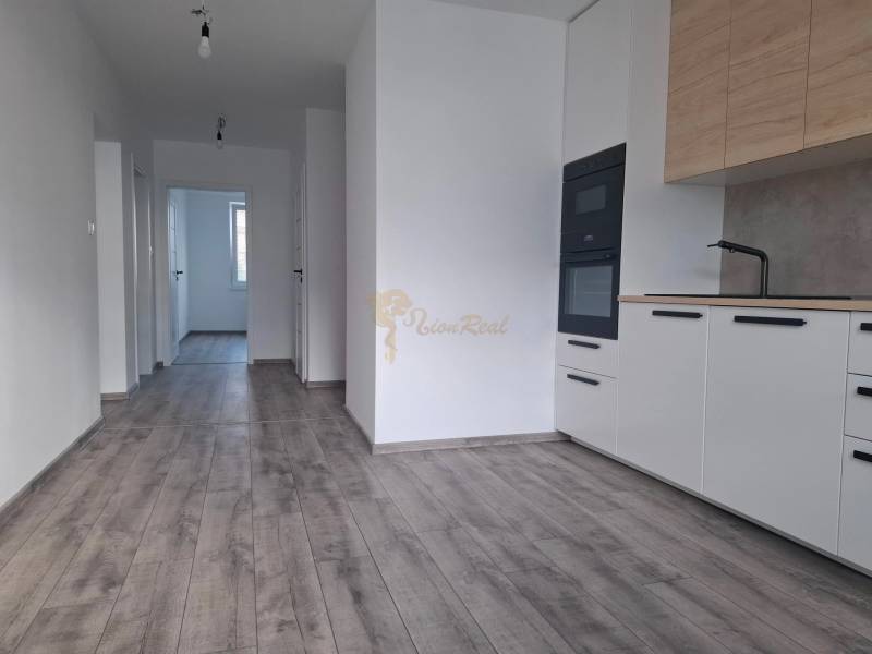 The kitchen of a 3-room apartment with white cabinets, a wooden decor floor, and a hallway.