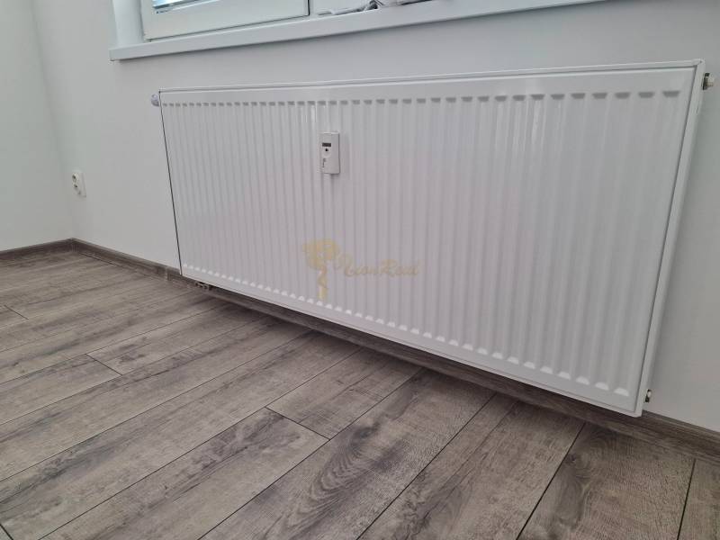 Radiator by a white wall, next to a floor with wood decor in a 3-room apartment.