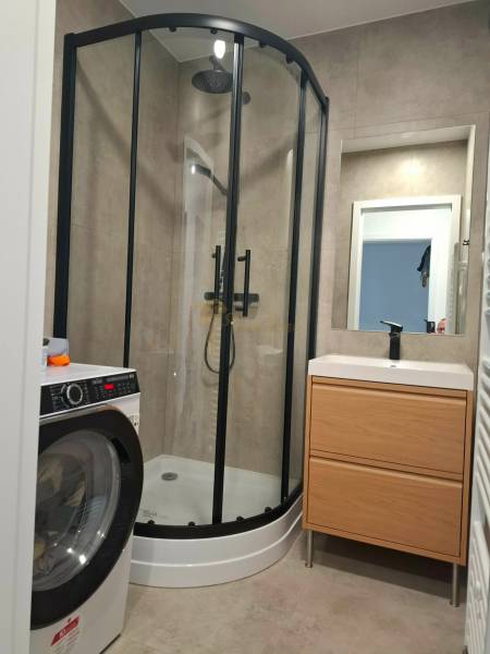 Bathroom in a 3-room apartment with a washing machine, shower, and sink with storage space.