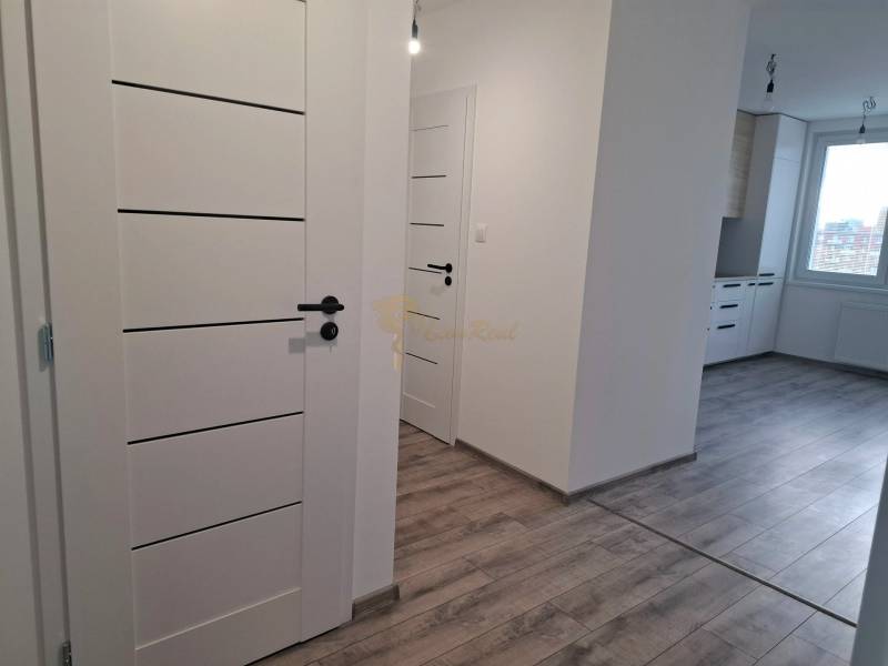 A white hallway with an entrance to the kitchen, a floor with a wood decor in a 3-room apartment.