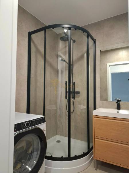 A bathroom with a shower, a washing machine, and a cabinet in a 3-room apartment.