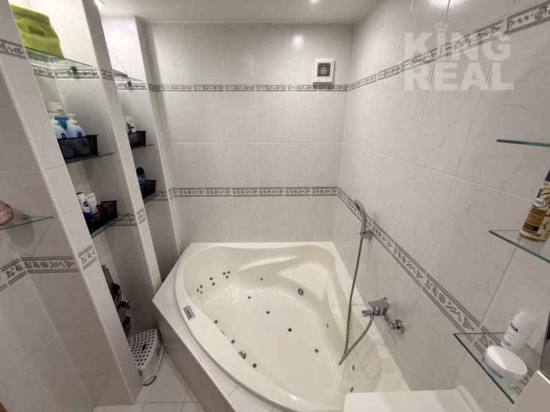 A bathroom in a 3-room apartment with a corner bathtub and shelves for cosmetics.