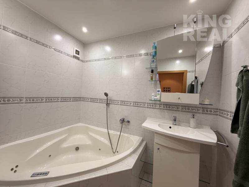 A bathroom with a bathtub and a mirror in a 3-room apartment. White tiles with a decor.