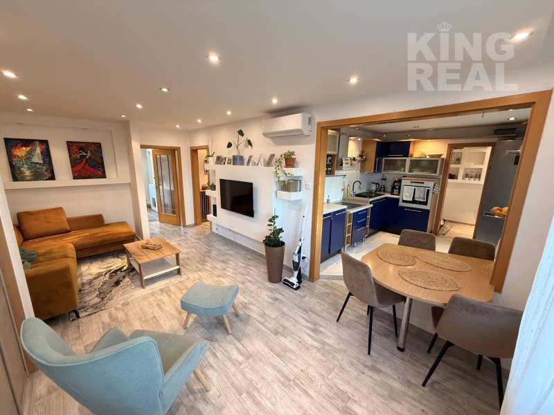 Living room with kitchen in a 3-room apartment, wooden decor flooring, comfortable seating.