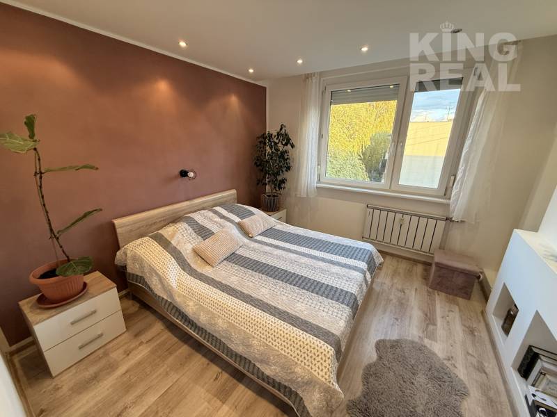 A bedroom in a 3-room apartment with a wooden decor floor and a plant next to the bed.