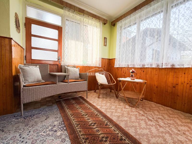 Interior of a family house with rattan furniture, floral curtains, and a carpet.