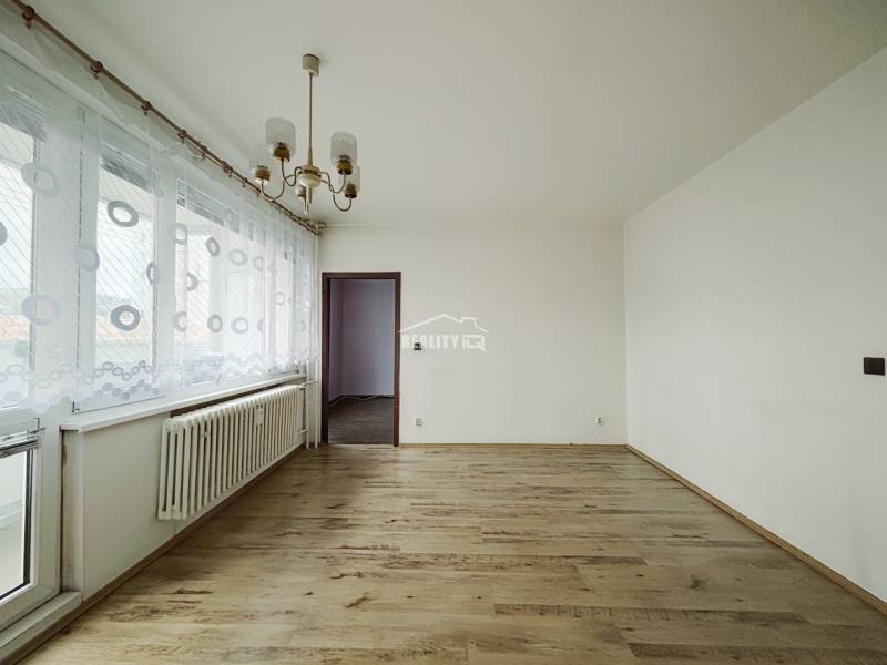 A room with a wooden floor decor and a chandelier in a three-room apartment.