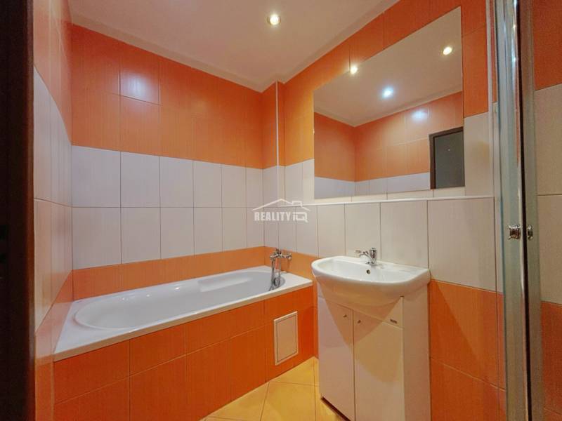 A bathroom with a bathtub and a sink in a 3-room apartment with orange and white tiles.