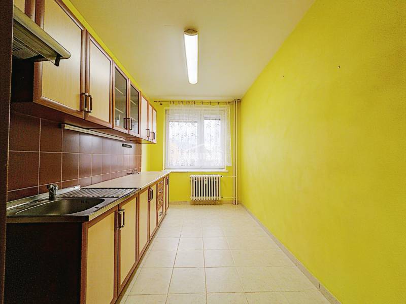 A kitchen in a 3-room apartment with yellow walls and brown tiles behind the counter.