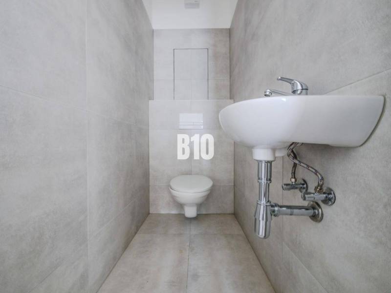 Bathroom with toilet and sink in a 3-room apartment, tiled with light tiles.