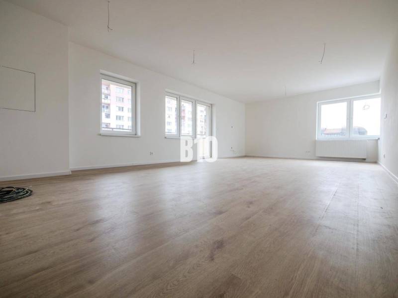 Spacious 3-room apartment with windows, wooden floor, and white walls.