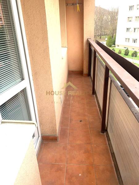 A balcony in a 2-room apartment with terracotta tiles and a view of greenery.