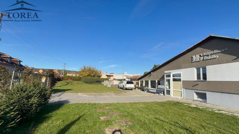 Commercial premises in Dolné Chlebany with a parking lot, landscaped greenery, and a blue sky.