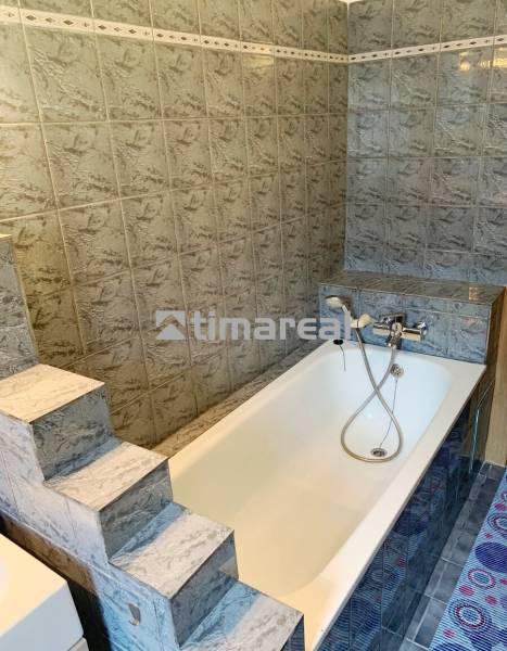 A bathroom with a bathtub in a 2-room apartment, tiled with patterned tiles.