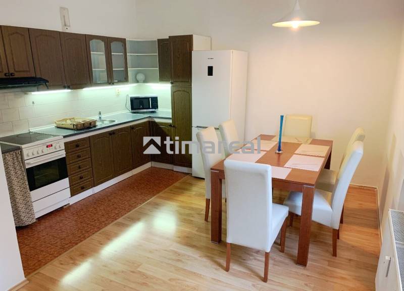 A kitchen in a 2-room apartment with a dining table, wooden cabinets, and a wooden decor floor.
