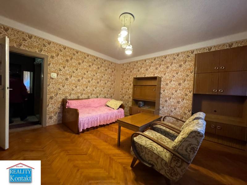 The living room in the family house has wallpapered walls, wooden furniture, and a floor with a wooden decor.