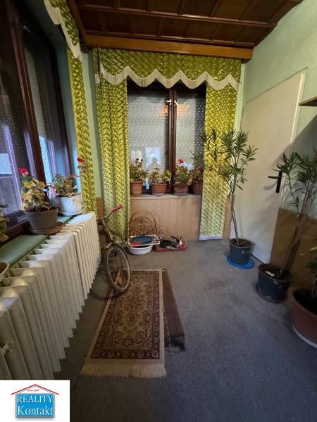 Interior of a family house with flowers, a bicycle, green curtains, and carpets.