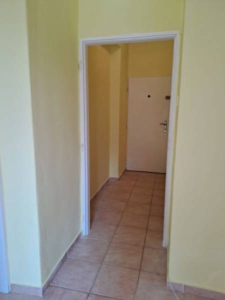A hallway in a one-room apartment with light tiles and yellow walls.