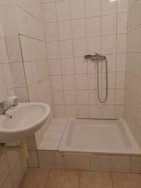 A bathroom with white tiles and a shower in a studio apartment.