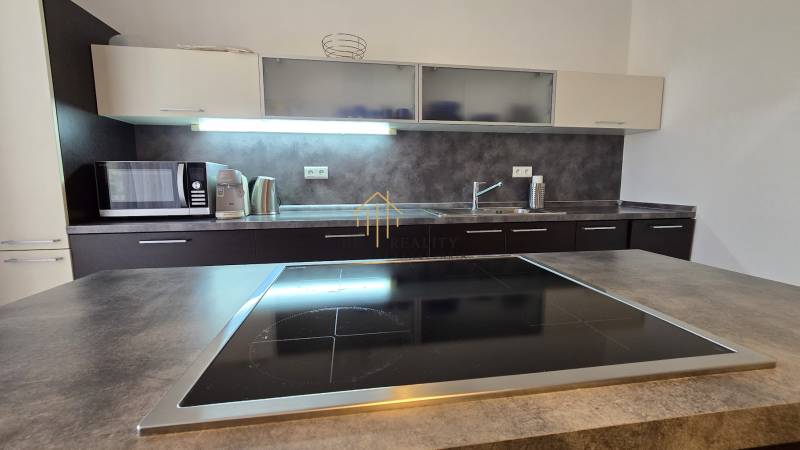 A kitchen in a 3-room apartment with a cooktop, microwave, and wooden decor of the countertop.