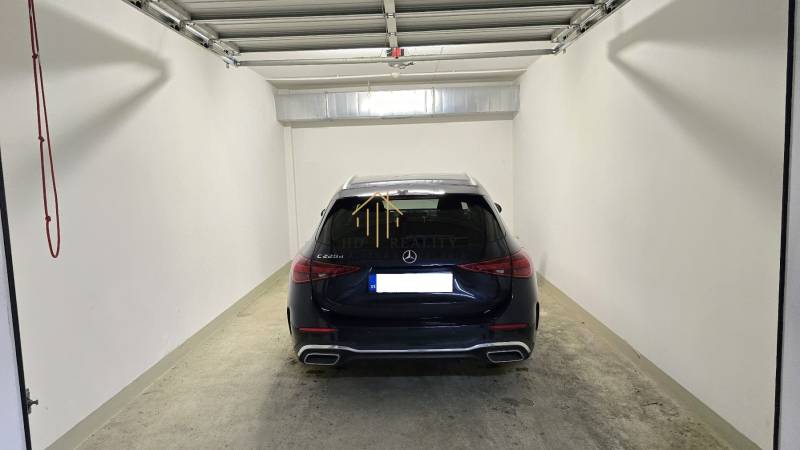 A garage with a Mercedes-Benz C223d with a concrete floor and white walls.