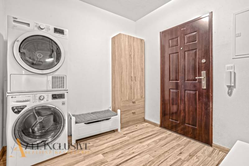 Entrance hall in a 3-room apartment with a washing machine, dryer, and wooden decor flooring.