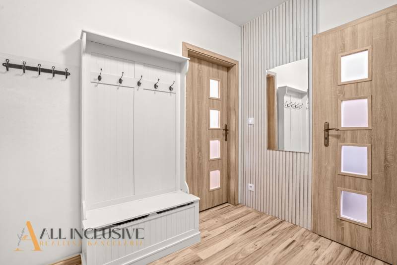 Entrance hall in a 3-room apartment with coat racks, a mirror, and a wooden decor floor.