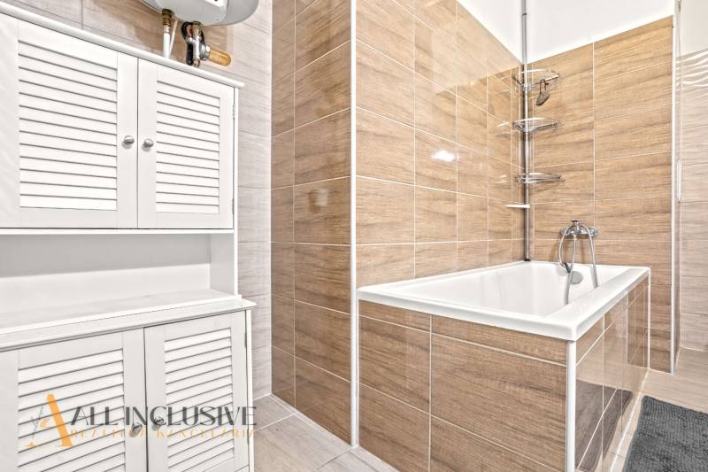 A bathroom with a bathtub, white cabinets, and tiles in a 3-room apartment.