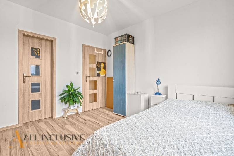 A bedroom in a three-room apartment with a wooden decor floor and simple furnishings.