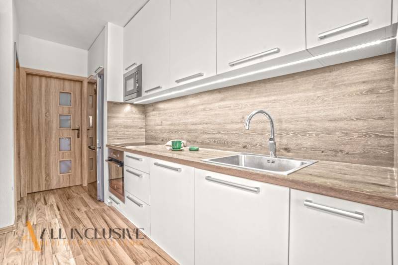 A kitchen with light cabinets, wood-patterned flooring, and a sink in a 3-room apartment.