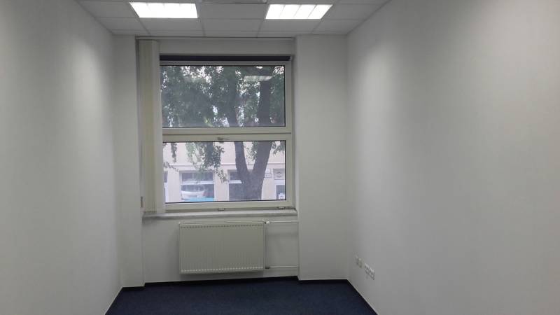 White office with a window, radiator, and blue carpet.