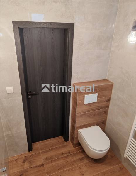 A bathroom in a three-room apartment with a wooden decor floor and a wall-mounted toilet.