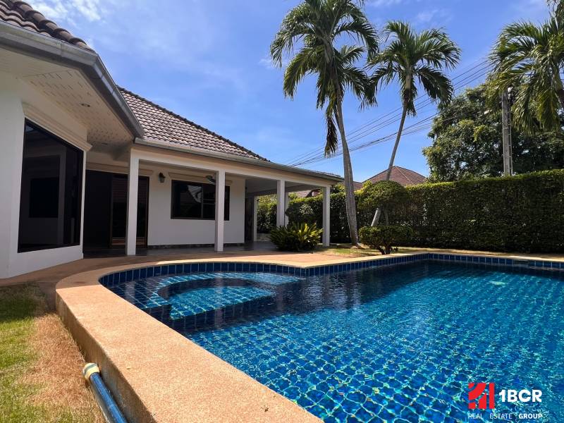 A villa in Pattaya with a garden and a pool, surrounded by palm trees and a hedge.