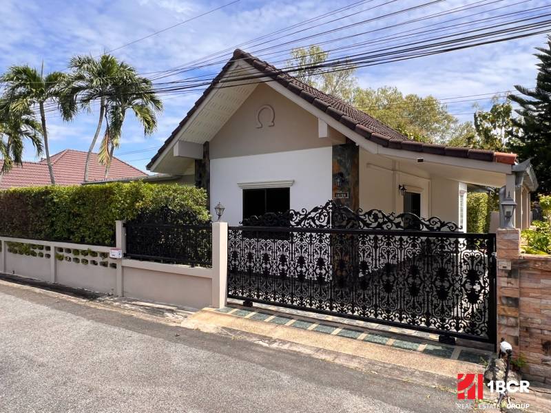 A villa in Pattaya with a decorative metal gate, surrounded by greenery and palm trees.
