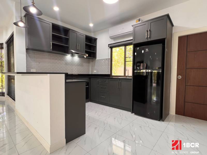 A kitchen in a villa with dark cabinets, white tiles, and a spacious floor.