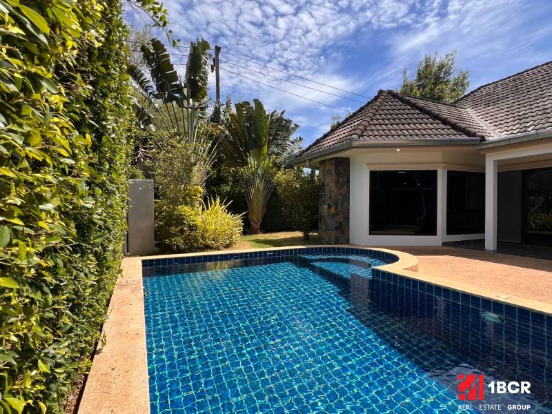 A villa in Pattaya with a pool surrounded by greenery and a blue sky.