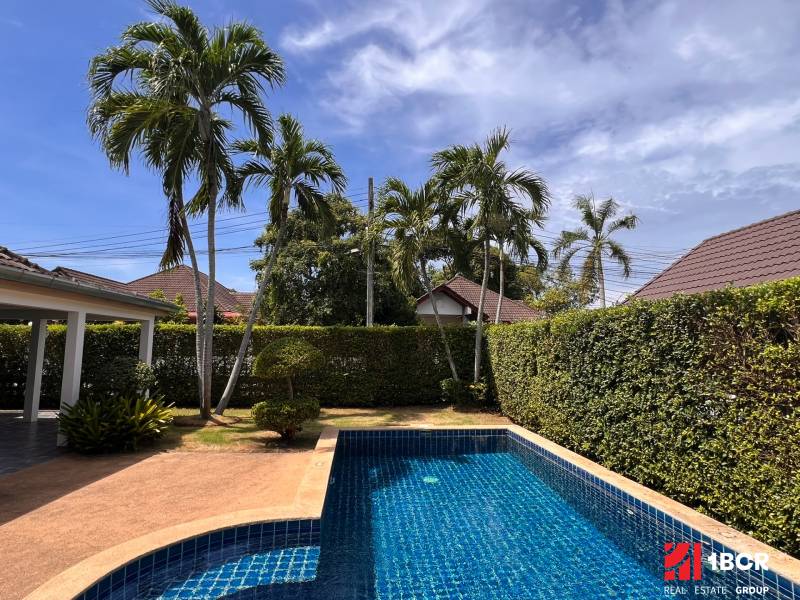 Villa in Pattaya with a pool, palm trees, and a landscaped garden on a sunny day.