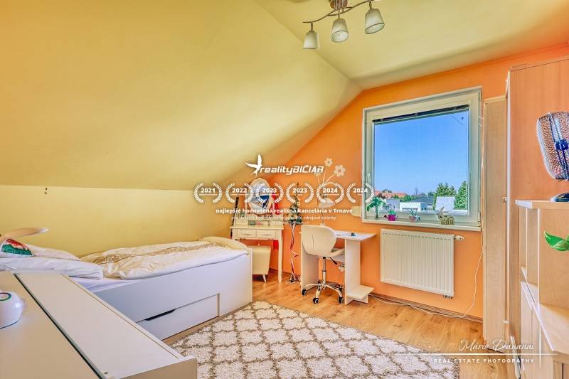 Attic room with a bed, a desk, and a wooden-patterned floor in a family house.