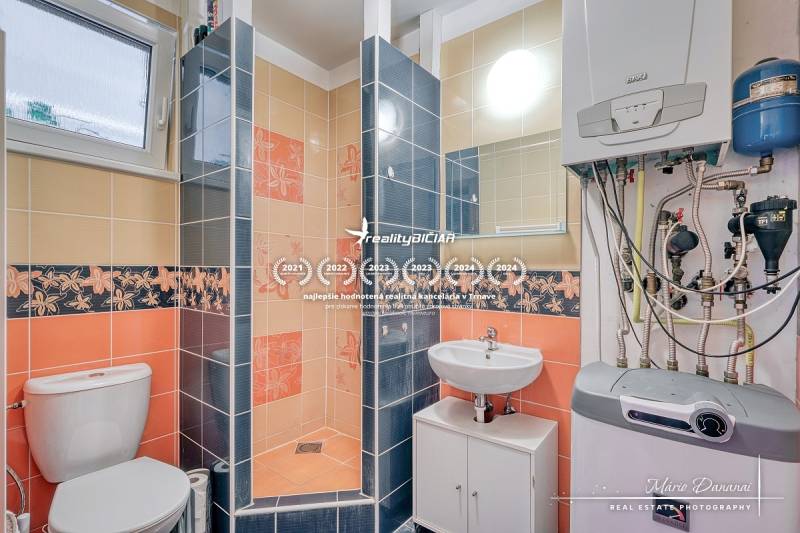 A bathroom in a family house with colorful tiles, a sink, a toilet, and a boiler.