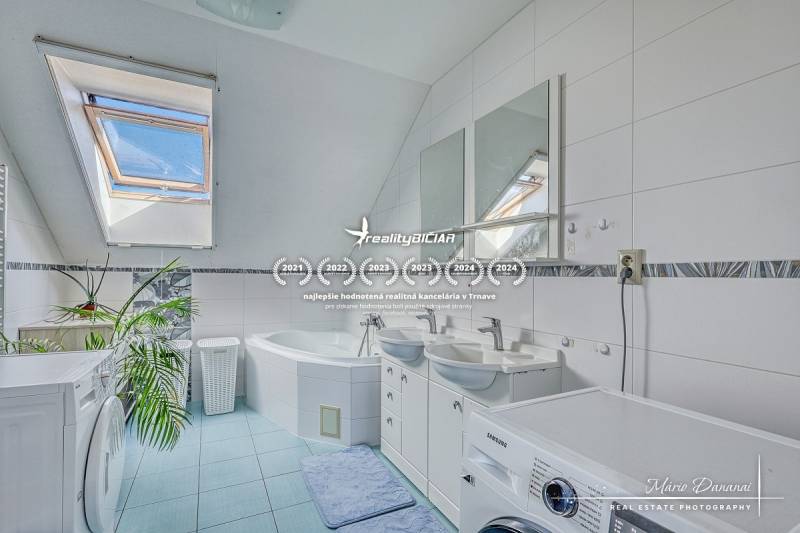 Bathroom with a window, bathtub, two sinks, and a washing machine in a family house.