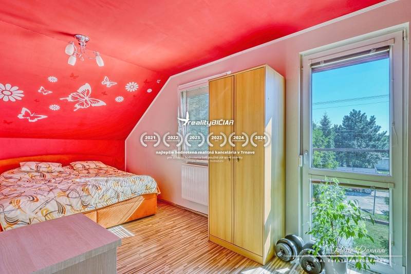 Bedroom in a family house with a red wall, window, and wood-patterned floor.