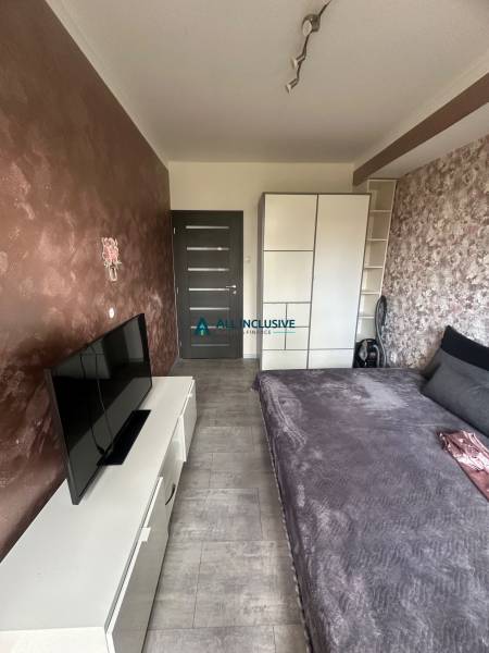 A bedroom in a two-room apartment with a television, a double bed, and a built-in wardrobe.