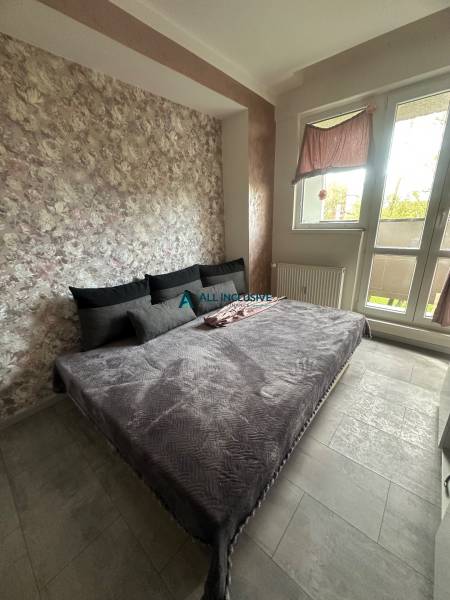 A bedroom in a studio apartment with a large bed, floral wallpaper, and ceramic flooring.