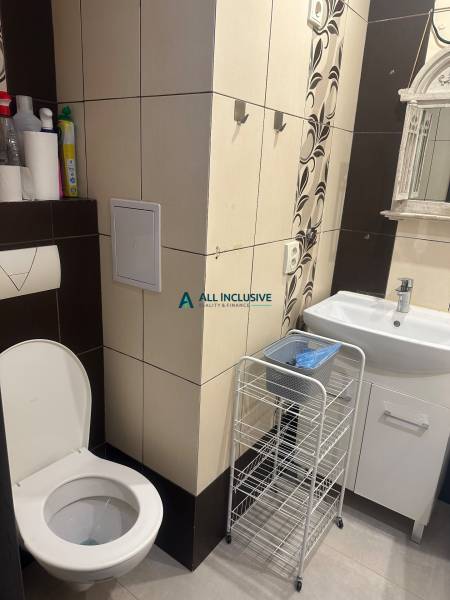 Bathroom in a studio apartment with a toilet, sink, and storage shelf.