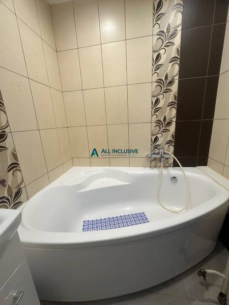 A bathroom with a corner bathtub and decorative tiles in a studio apartment.