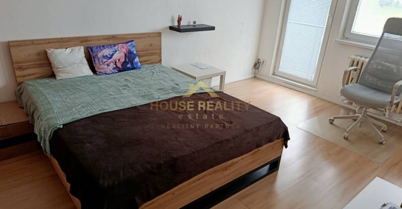 A bedroom in a studio apartment with a bed, an armchair, and a wooden decor floor.