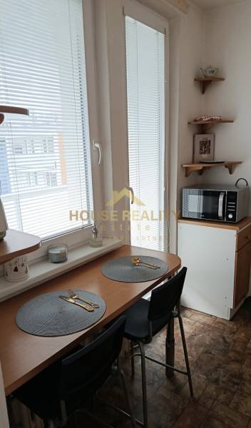 A kitchen with a dining area, a microwave, and windows with blinds in a studio apartment.