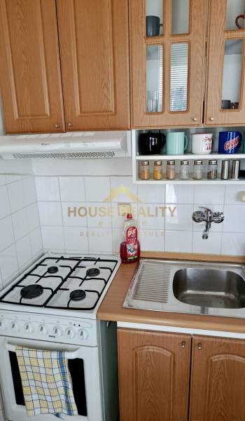 A kitchen in a studio apartment with a gas stove and wooden cabinets.