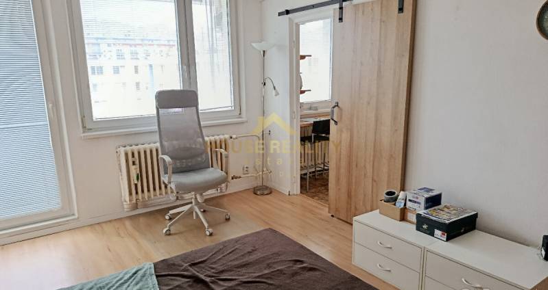 Interior of a 1-room apartment with a wooden decor floor, an armchair, and sliding doors.
