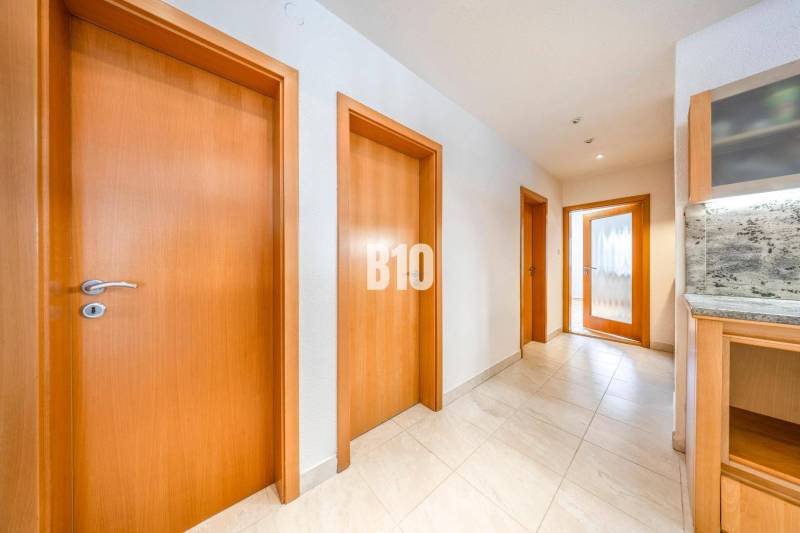 A hallway in a 3-room apartment with multiple doors and light-colored tiles.